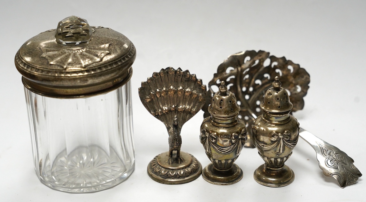 Three assorted modern silver wine labels, a ceramic wine label, a pair of silver pepperettes, a silver topped glass toilet jar, a Dutch white metal sifter spoon and seven plated items including a pair of peacock menu hol